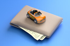 Toy car on top of wallet Toy car sitting on top of wallet with corners of bills sticking out from wallet blue background