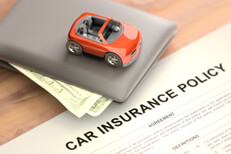 Toy car with wallet and insurance policy Toy car sitting on top of wallet with car insurance policy papers on wood table