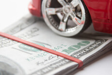Car insurance cost Close view of chrome car wheel and tire resting on folded 100 dollar bills with rubber band