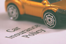 Small yellow toy car angled on car insurance policy paperwork