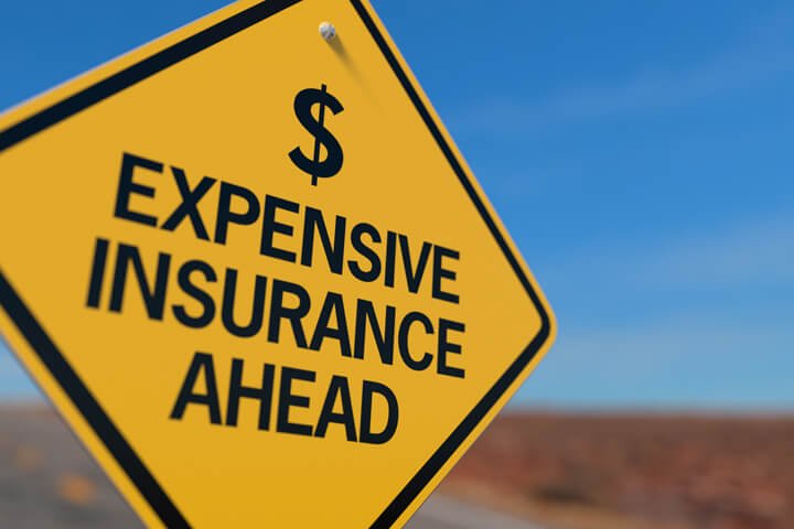 Yellow road sign reading Expensive Insurance Ahead with dollar sign icon
