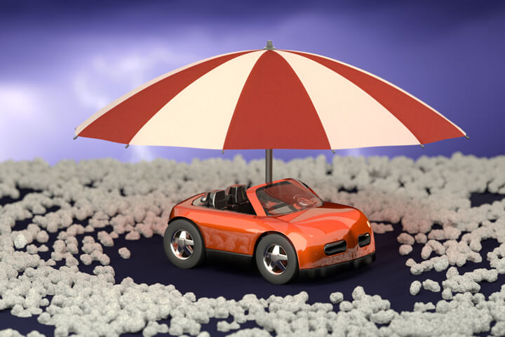 Red toy car with umbrella surrounded by hail stones with stormy sky background