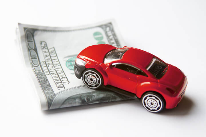 Toy car climbing stack of folded money automotive cost or cost of insurance concept