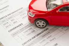 Red car on car insurance policy Red toy car on a car insurance policy showing vehicle and driver information and coverages