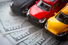 Three toy cars on money Photo of black, yellow, and red toy cars on fanned out 100 dollar bills