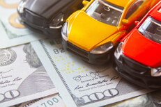 Photo of black, yellow, and red toy cars on scattered 100 dollar bills