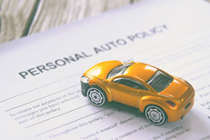 Toy car on personal auto insurance policy on wood background