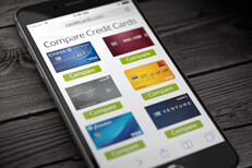 Compare credit cards on cell phone Mobile phone on weathered wood desk showing website comparing different credit cards
