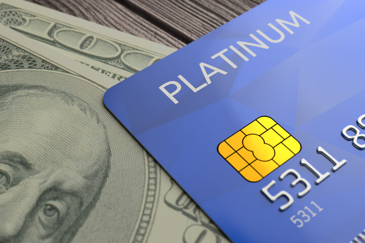 Blue platinum credit card lying on top of one hundred dollar bill