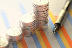 Coins and pen on investment column chart Investment column chart on paper with stacks of coins and pen laying on top