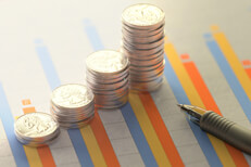 Stacks of coins on column chart Column chart showing investment returns with increasing stacks of coins and ballpoint pen
