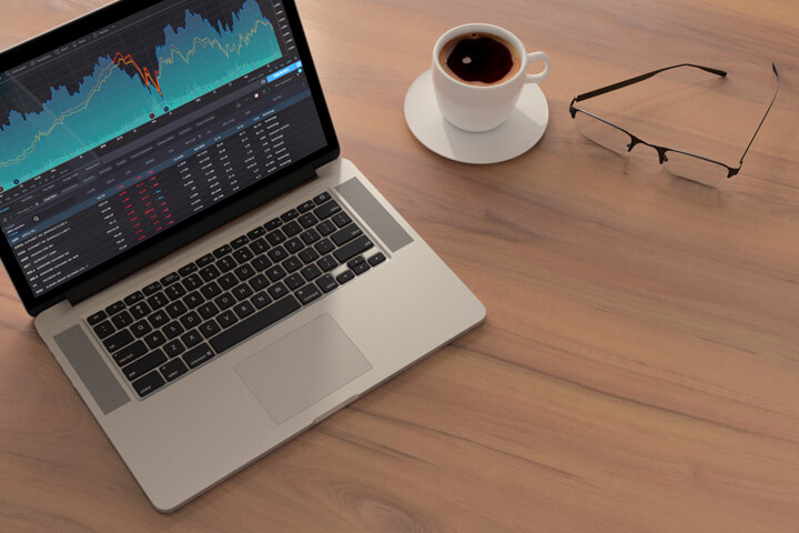 Laptop with stock price information showing on table with coffee and reading glasses