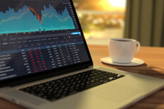 Laptop on table in morning light with stock trading screen and coffee cup