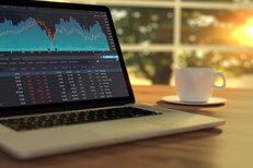 Laptop with stock picks in morning Laptop on table with sunrise showing stock prices and area chart
