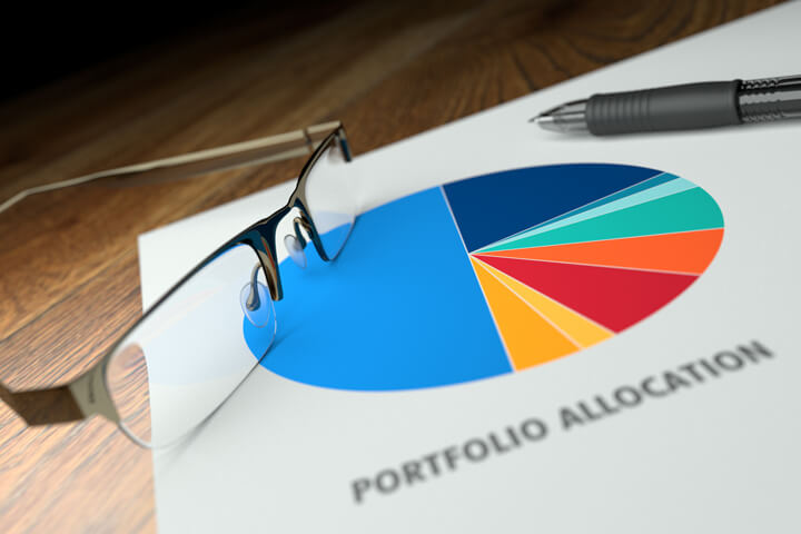 Paper on desk showing pie chart of portfolio allocation with reading glasses and ballpoint pen