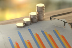 Investment returns with coin stacks Paper showing investment return column chart with increase stacks of quarters and reading glasses