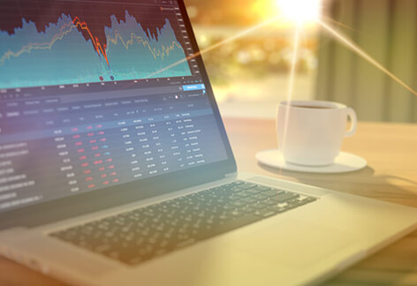 Laptop on table at sunrise showing stock price information