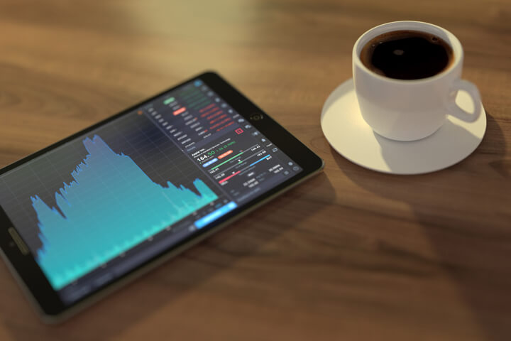 Table with iPad showing stock price information, investment portfolio, and cup of coffee