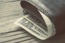 Vintage photo of leather wallet with dollar bills sticking out on wood background