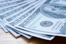 Fanned out $100 bills with shadow $100 bills evenly fanned out on wood with hard shadow