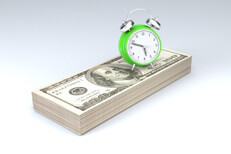 Green clock on stack of money Clock sitting on stack of money concept image for time is money, time value of money, or retirement