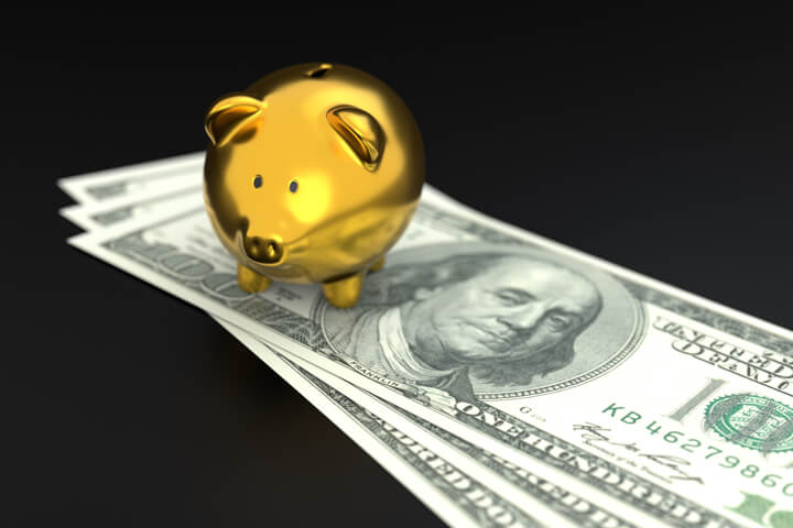 Gold piggy bank sitting on 100 dollar bills on dark background