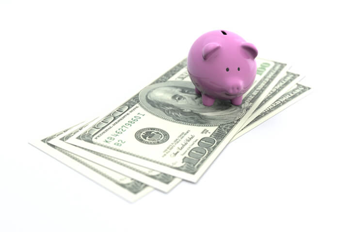 Small pink piggy bank on three 100 dollar U.S. bills concept image for savings, retirement, or investment