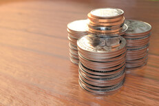 Large stacks of coins wood Three large stacks of shiny quarters with other smaller coins on top with rich wood surface