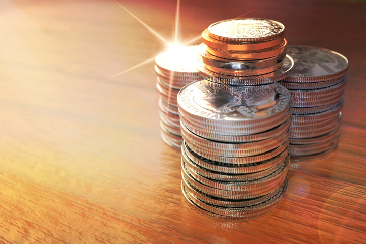 Three large stacks of shiny quarters with other smaller coins on top with lens flare and strong sun burst highlight