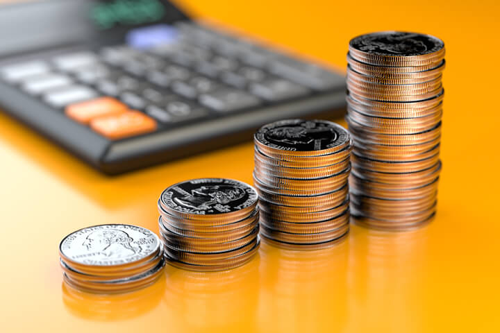 Four increasing stacks of U.S. quarters in front of calculator on orange reflective background