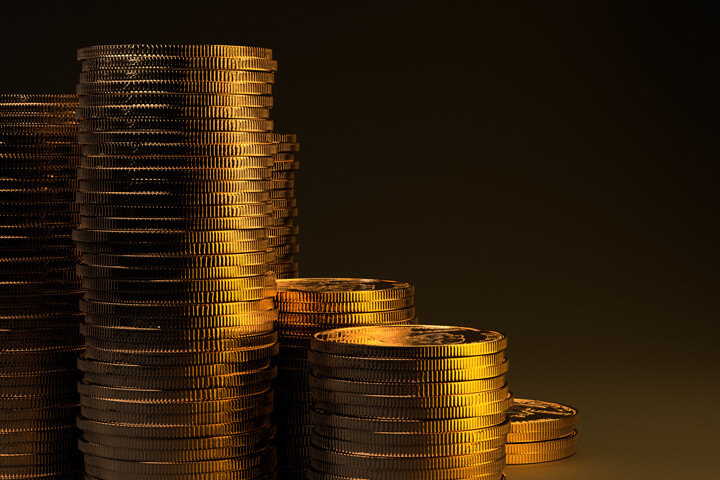 Large stacks of gold coins on dark background with gold lighting