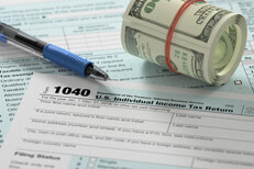Tax forms with cash roll Bundled roll of 100 dollar bills on top of IRS form 1040 with ballpoint pen