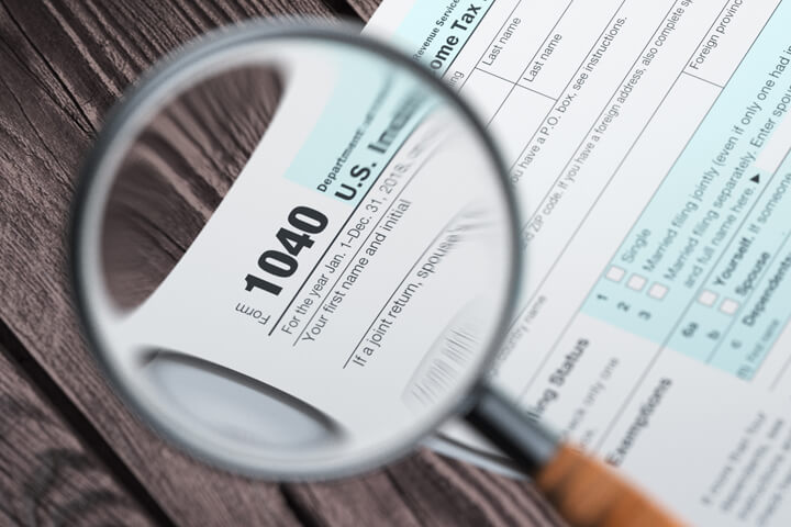 IRS form 1040 magnified in magnifying glass on wood plank background