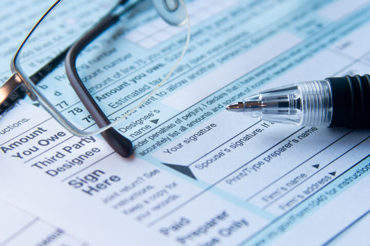 IRS form 1040 signature line close up with reading glasses and ballpoint pen