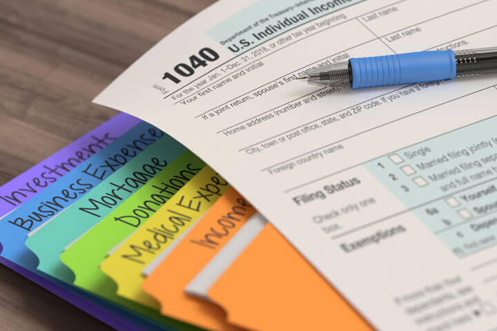 Colorful stacked tax manila folders with 1040 form and ballpoint pen on top