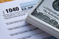 Stack of cash on tax form Large bundle of 100 dollar bills on IRS form 1040 concept for paying high taxes