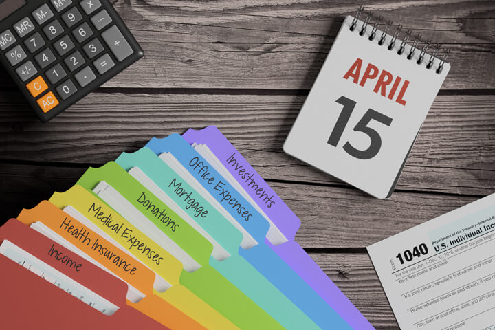 Wood plank background with April 15th calendar, calculator, tax category folders, and 1040 IRS form