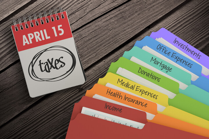 Overhead view of day calendar showing April 15th with colorful tax category folders fanned