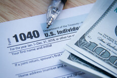 Tax form with money IRS form 1040 with stack of 100 dollar bills and ballpoint pen