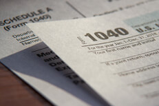 1040 Schedule A Photo of IRS 1040 tax form lying on top of Schedule A form with hard shadow