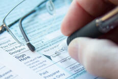 Close view signing 1040 tax form Photo of hand holding pen signing tax form with reading glasses