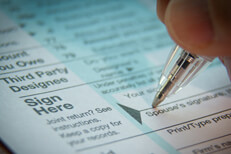 Signing tax form Vignetted close up photo of signature with ballpoint pen on IRS tax form