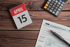Desk scene with tax items April 15 day planner calendar with calculator and IRS form 1040 on wood background