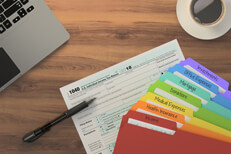Tax prep with laptop and folders Overhead desk view of laptop, coffee, 1040 form, and rainbow-colored tax category folders