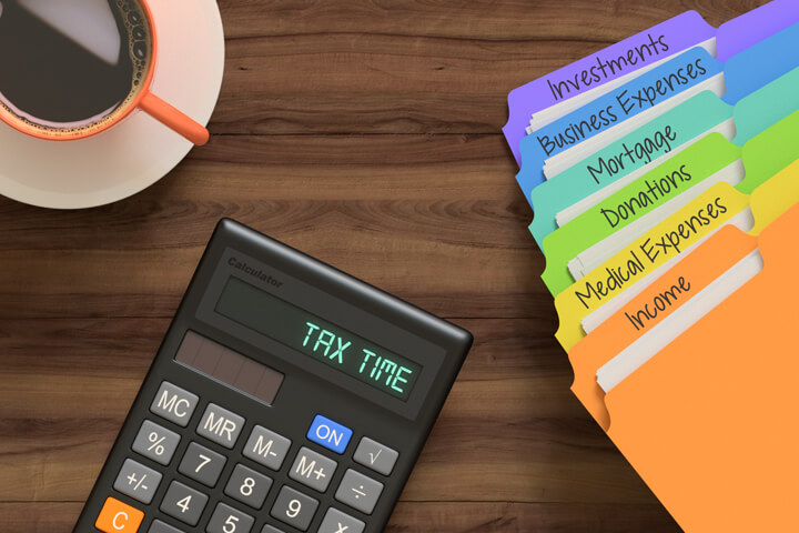 Desk top view showing rainbow-colored tax category folders, calculator, and cup of coffee
