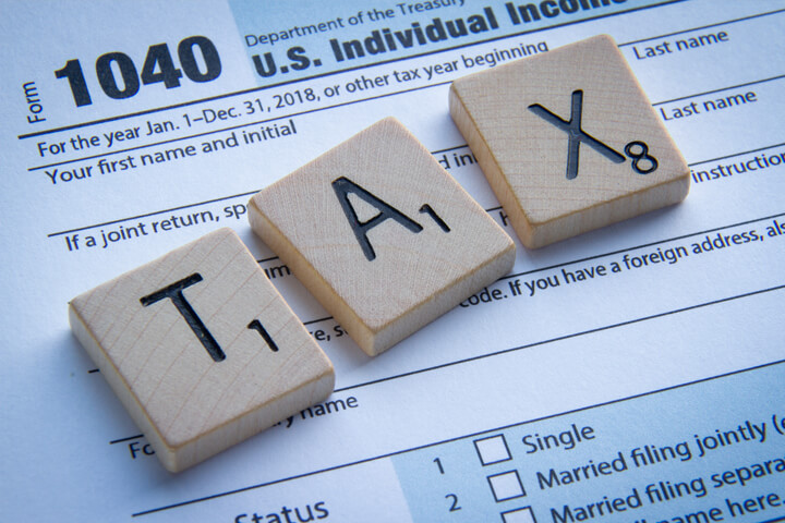 Wooden Scrabble letters spelling TAX on IRS form 1040