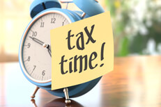 Old style alarm clock on table with sticky note reminder that says tax time