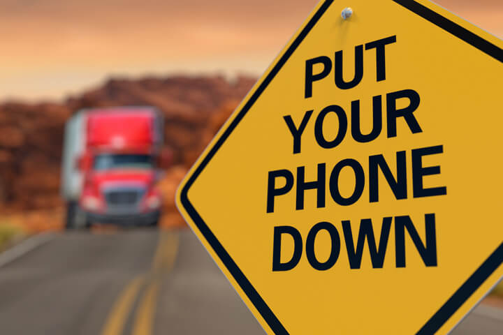 Yellow road sign reading Put Your Phone Down with oncoming semi truck on highway burred in background
