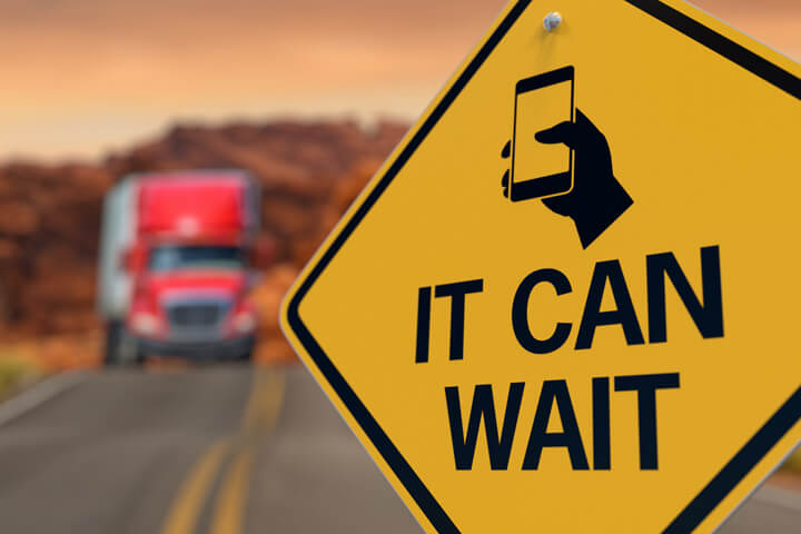 Road sign reading It Can Wait with texting icon and oncoming semi truck blurred in background